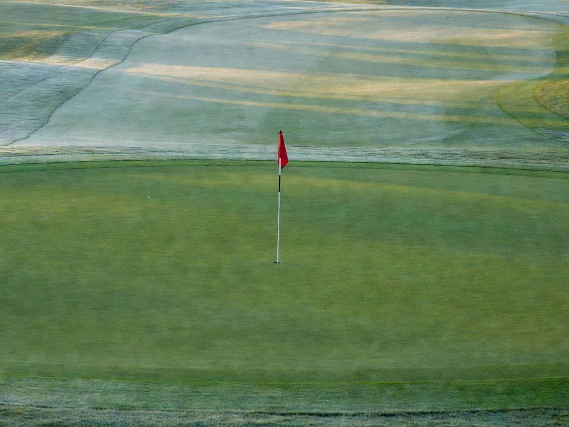 A golf flag positioned on a manicured green with soft morning shadows on the fairway